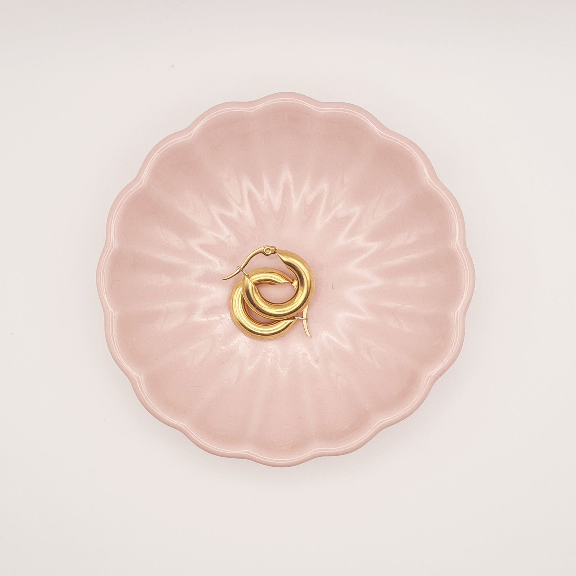 Small chubby hoop earrings in 18K gold-plated stainless steel by Forge and Lumber on a pink plate.
