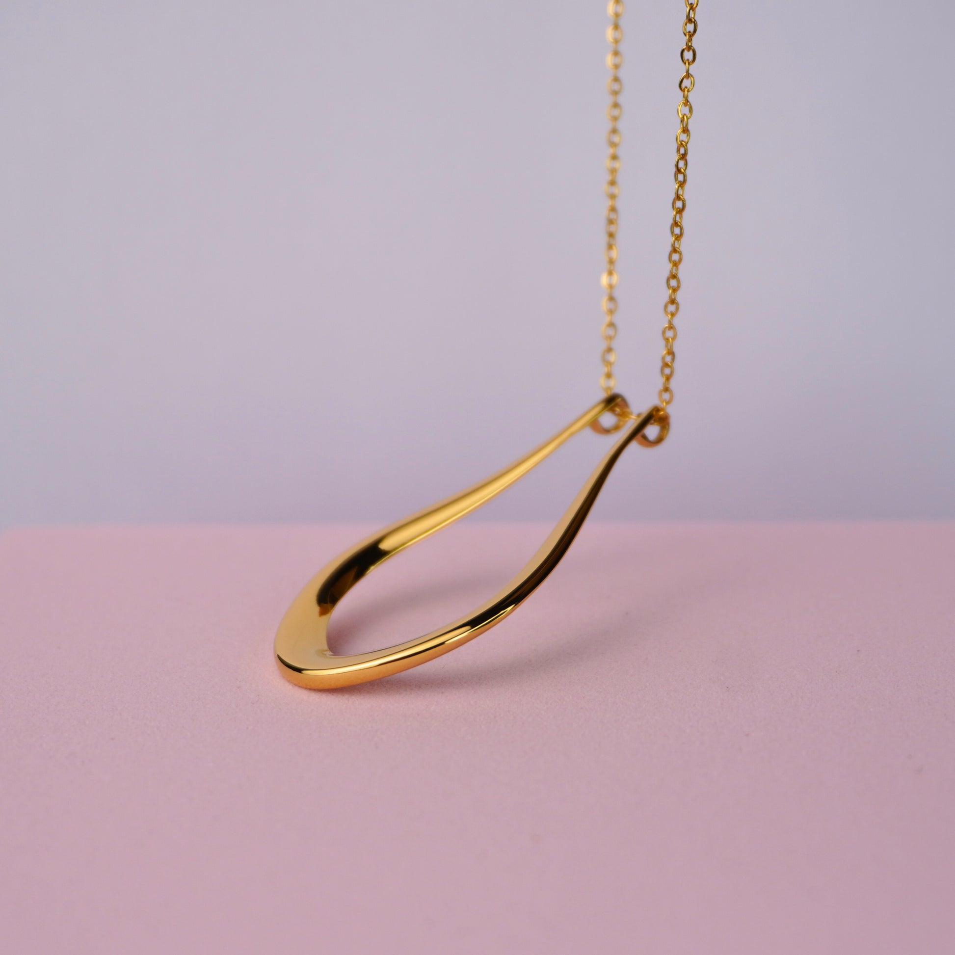 Gold teardrop pendant necklace on a delicate chain against a pastel background.