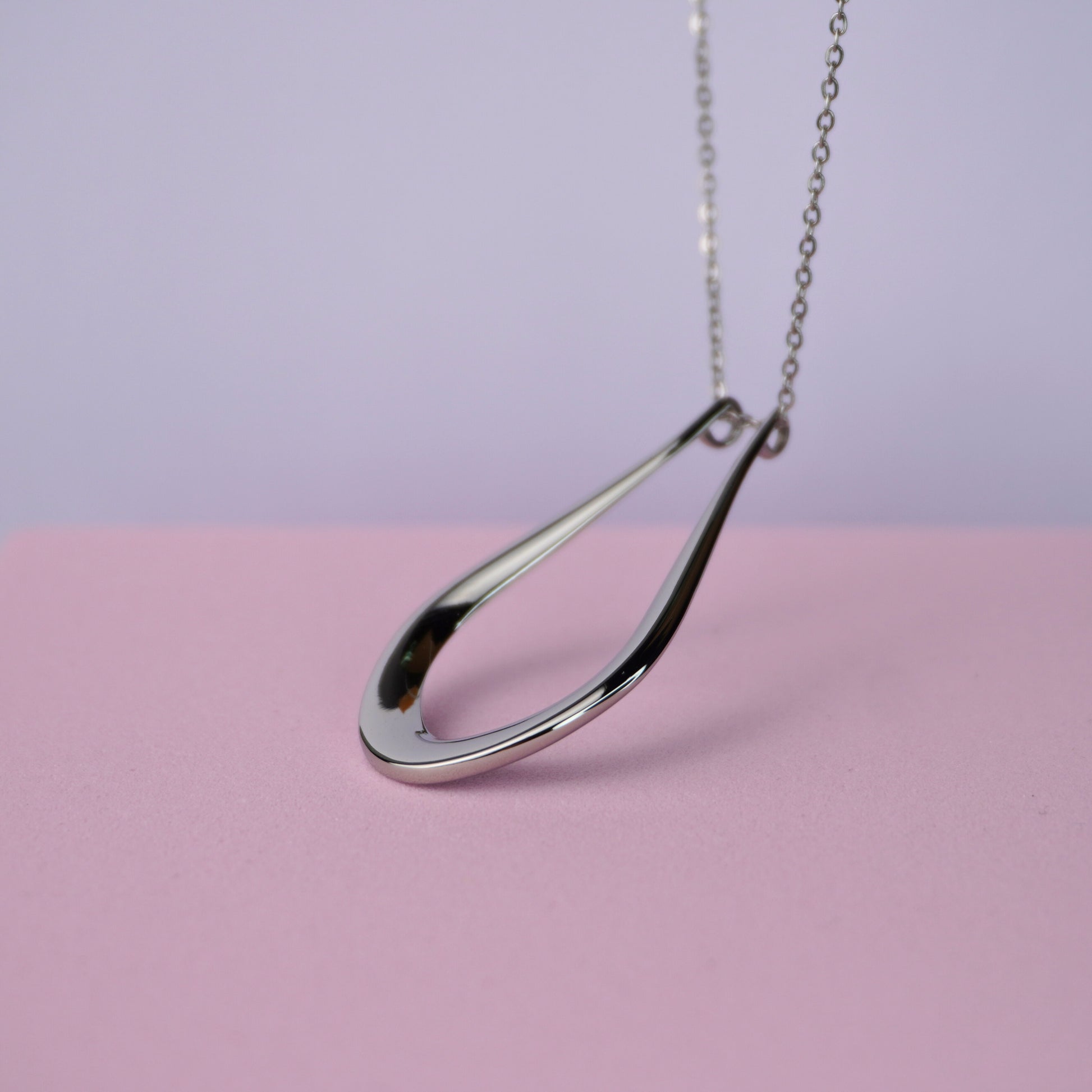 Silver teardrop pendant necklace on a delicate chain against a pink background.