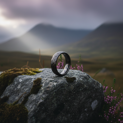 Black 6mm anniversary ring with anvil-inspired design by Forge and Lumber, set on a textured rock backdrop.