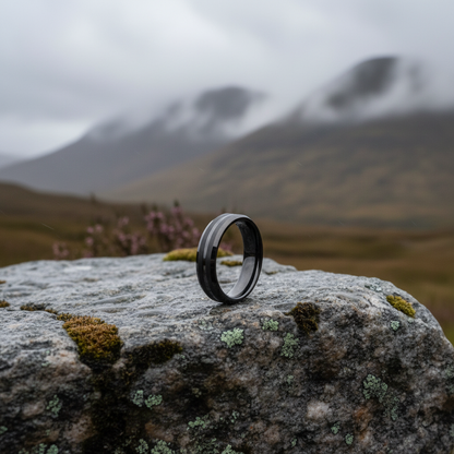 Black beveled 6mm wedding band ring by Forge and Lumber, displayed on a rocky surface in a natural setting.