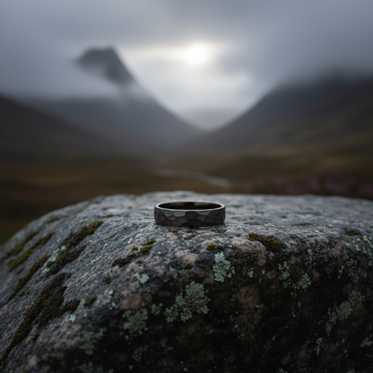 Black anvil-inspired ring by Forge and Lumber, 6mm width, on mossy stone backdrop with misty mountains.
