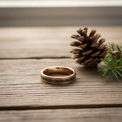 Rose gold 4mm wedding band with a textured black inlay by Forge and Lumber, set on a wooden surface with pinecones.
