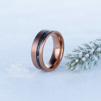 Rose gold 8mm wedding band with a black inlay by Forge and Lumber set on snowy background.