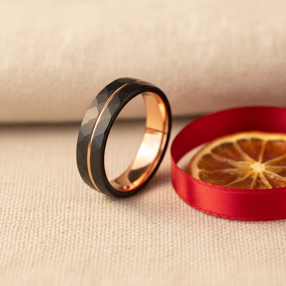 Sleek black and rose gold faceted ring beside a red ribbon and dried orange slice, showcasing "The Bonnie."