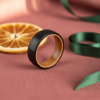 Black matte ring with a wooden interior, placed on a pink fabric background with dried orange and green ribbon.