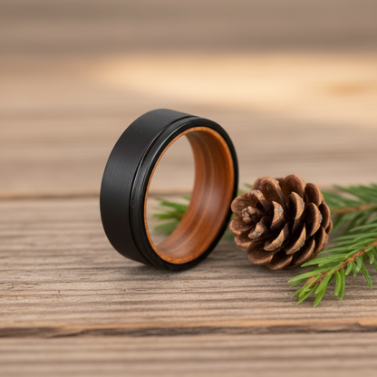 Sleek black 8mm ring with a wooden interior, placed on rustic wooden surface with pinecone and greenery.