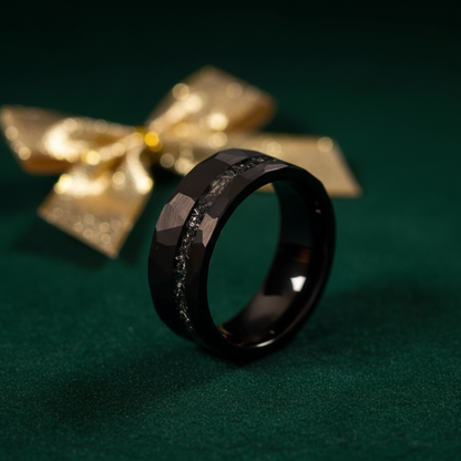 Black faceted ring with a textured band, set against a green background and gold bow, perfect for gifting.