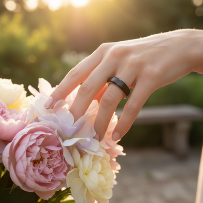 Beveled black barrel-wood ring by Forge and Lumber, worn on hand near pastel roses.