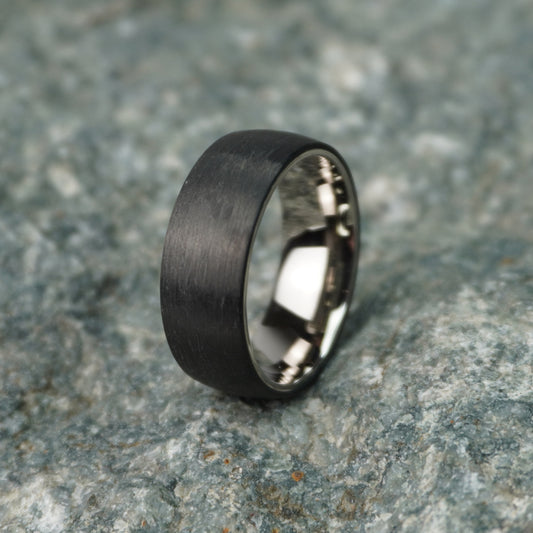 Black 8mm carbon fiber ring with a brushed finish by Forge and Lumber, suitable for weddings and anniversaries.