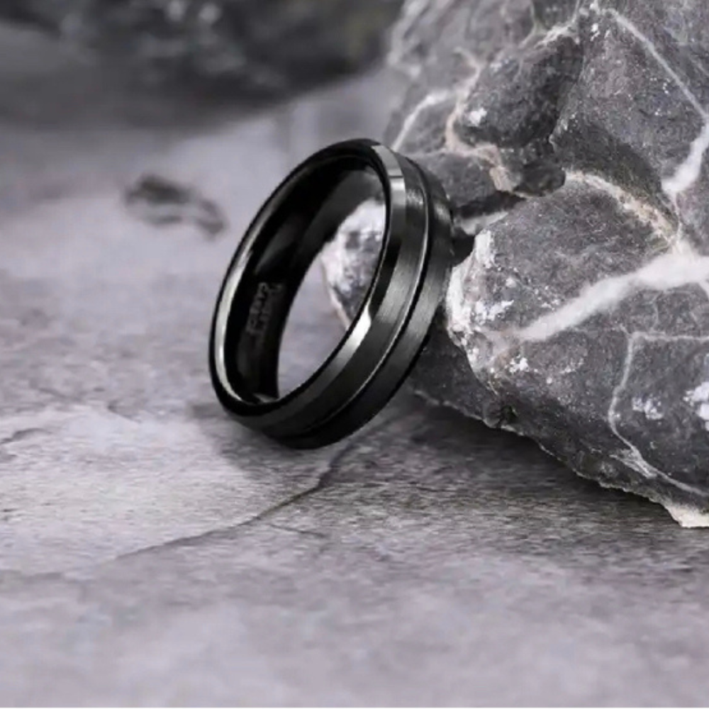 Black brushed tungsten wedding band, 6mm beveled design by Forge and Lumber, set against a rocky background.